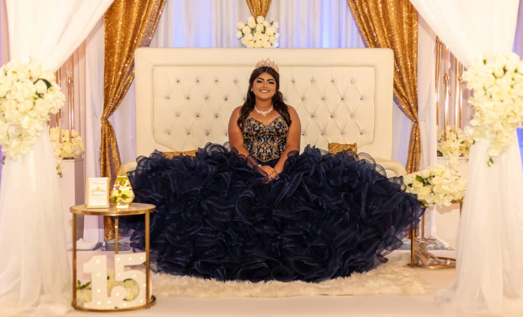 Woman in a black gown posing regally on a luxurious bed.